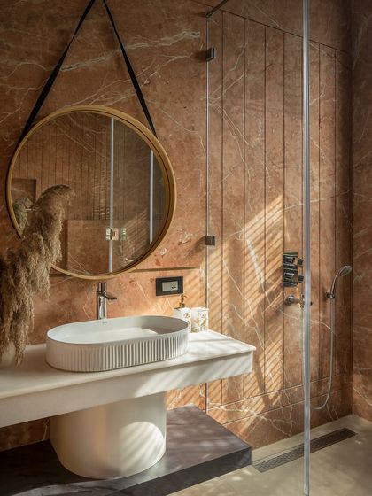 A terracotta retreat where rich stone balances raw textures with modern details. The ribbed shower walls add depth, while the round, strap-suspended mirror introduces a contemporary edge.