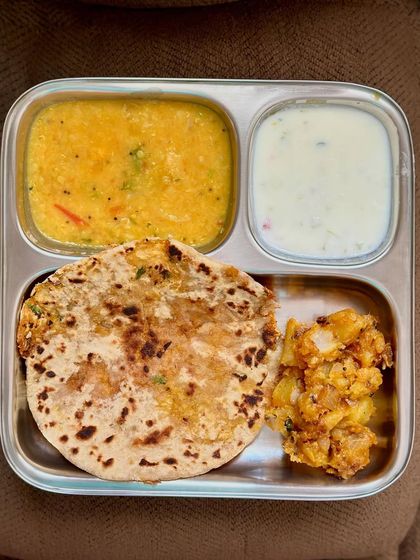 A comforting meal of stuffed cauliflower paratha with dal, sautéed potato, and raita.