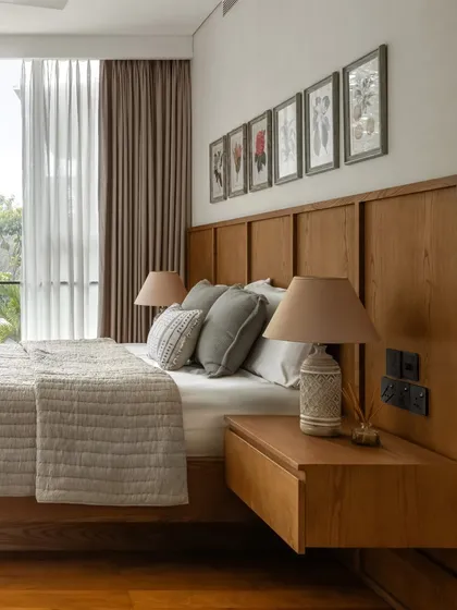 This bedroom feels soft and personal, with a wood headboard grounding the space and botanical prints adding a touch of nature.