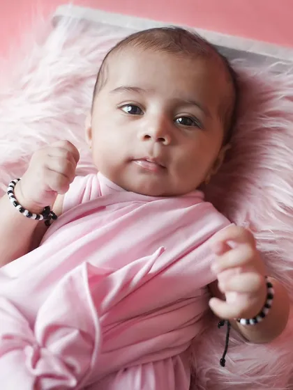 A beautiful three-month-old baby girl looking right at the camera. The simple pink setup highlights her lovely features.