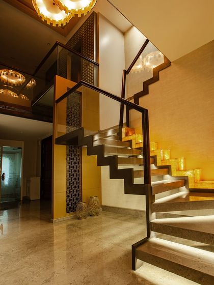 A modern floating staircase featuring stone treads and ambient under step lighting. The design is framed by sleek glass and wood railings, with a classic trellis pattern in the backdrop for a timeless touch.