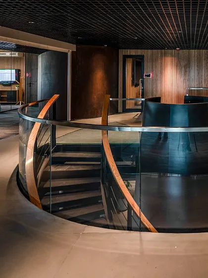 The curved glass balustrade of the central staircase at BCG HQ reflects the surrounding wood and metal textures, creating a sense of continuous, flowing movement.