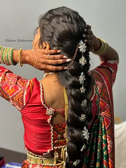 A stunning and unique bridal braid for a Gujarati wedding ceremony. The hair is styled in a thick braid and decorated with beautiful silver floral accessories.