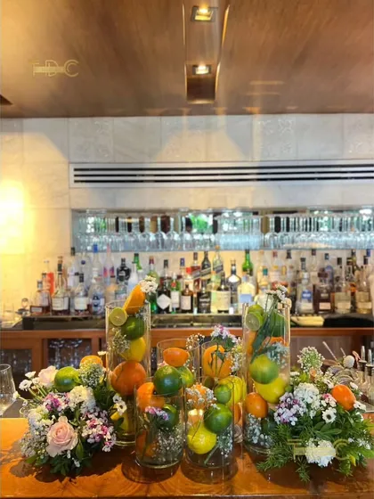 A fresh and zesty bar decoration for a summer birthday party. We filled tall glass vases with citrus fruits like lemons and oranges, interspersed with bright floral arrangements, to create a vibrant and cheerful atmosphere.