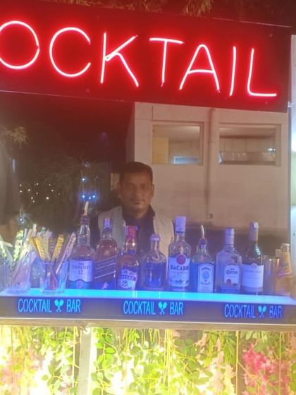 Our bartender posing at a floral-decorated cocktail bar, ready for a daytime wedding event.