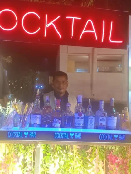 Our bartender posing at a floral-decorated cocktail bar, ready for a daytime wedding event.