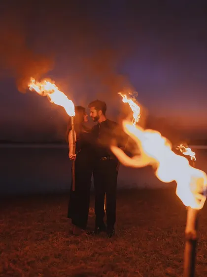 A dramatic pre-wedding shoot at dusk, using fire torches to create a powerful and romantic atmosphere by the water.