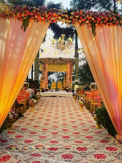 A view down the aisle towards the mandap, framed by a beautiful entrance arch. The peach drapes and floral arrangements create a warm and welcoming path for the bride's entrance.