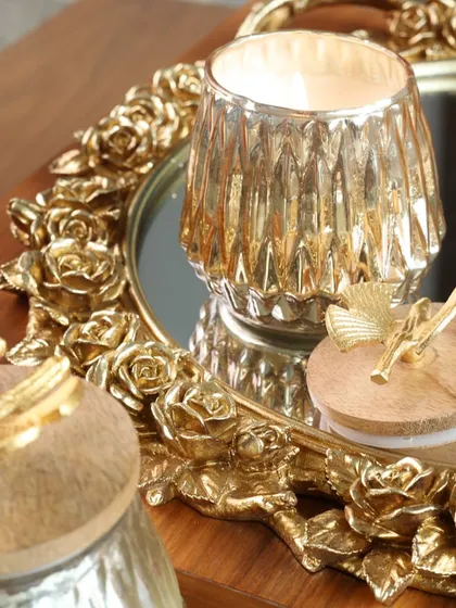 A golden votive holder with a textured glass finish, placed on our rose-bordered mirror tray. This pairing creates a romantic and opulent feel, perfect for a special occasion.