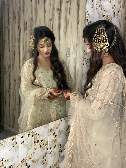 A quiet moment of reflection for the bride. Her hair is styled in soft waves with a traditional passa and maang tikka, perfectly complementing her elegant outfit.