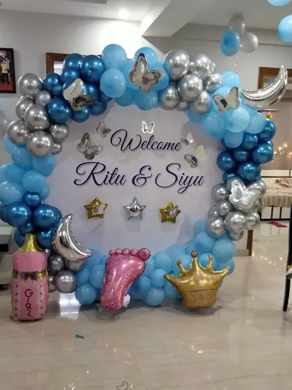A celestial themed welcome for baby Siyu. This beautiful setup includes a circular backdrop with a personalized "Welcome Ritu & Siyu" message, surrounded by a blue and silver balloon arch with moon and star foil balloons.
