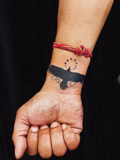 A solid black crow tattoo designed to cover up an old wrist piece. The abstract elements around the bird help to further obscure the original tattoo.