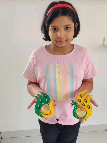 A proud young girl holding up the pair of peacock T-light holders she created, ready for the festival of lights.