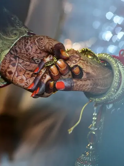 A macro shot of the couple holding hands during a wedding ritual, emphasizing their connection and the intricate details of their attire and mehendi.