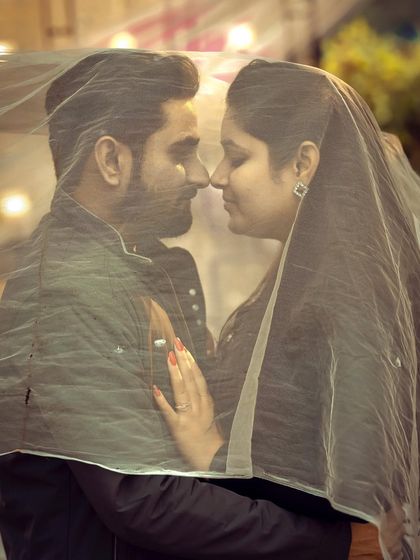 A classic romantic pre-wedding shot with the couple under a sheer veil, creating an intimate and dreamy portrait.