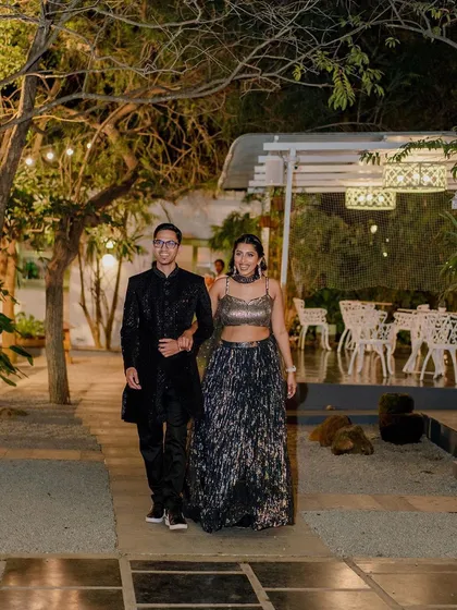 An elegant couple walks along the stone path at night. The ambient lighting from the trees and the covered dining area creates a sophisticated atmosphere for an evening event.