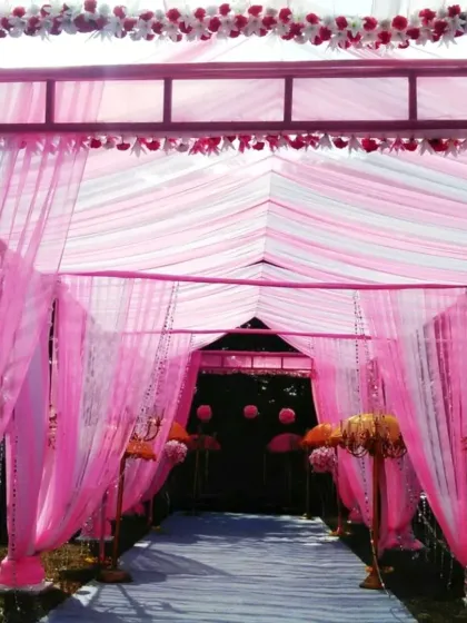 A beautiful entrance passage created with a metal frame and draped with flowing pink fabric, perfect for a daytime garden wedding.