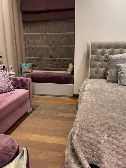 This shot highlights the cozy window seat, a perfect reading nook. The combination of the plush purple upholstery and the textured roman blinds adds another layer of comfort and style to the room.