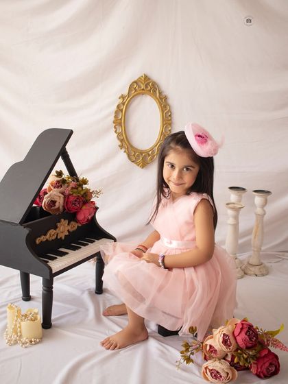 A classic and elegant fifth birthday portrait featuring our miniature grand piano prop. The soft pink dress and floral accents add a touch of sweetness.