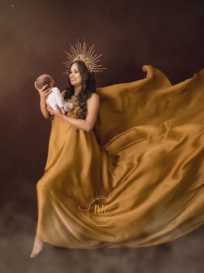 A goddess-like portrait of a mother holding her newborn, wearing a flowing golden gown and a sunburst crown.
