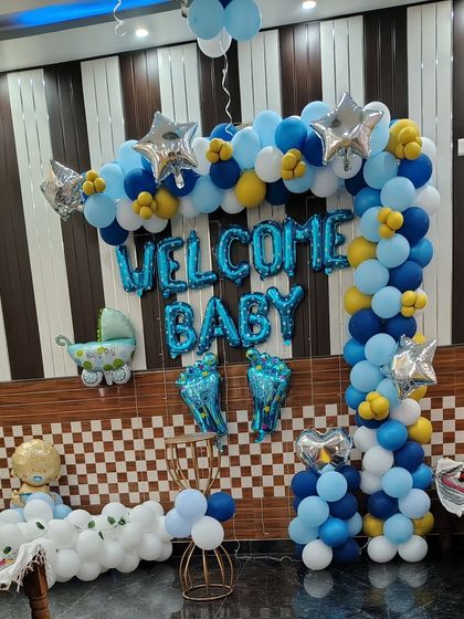 A full backdrop for a 'Welcome Baby' party. This setup features a blue, white, and yellow balloon arch, foil letters, and other baby-themed foil balloons.