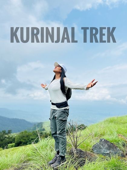 A trekker feeling on top of the world at the summit of Kurinjal, with arms outstretched to embrace the stunning landscape.