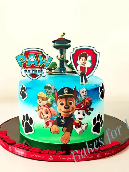 An airbrushed Paw Patrol cake with a vibrant blue and green background. The edible images of the pups make it look like they are jumping right out of the cake.