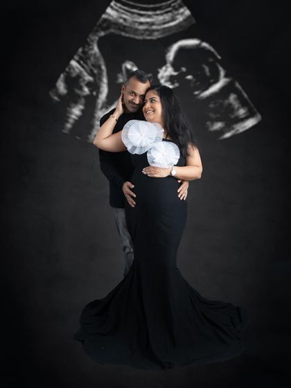 A creative couple's portrait with their baby's ultrasound scan projected in the background. It's a modern and meaningful way to include the newest family member in the photo.