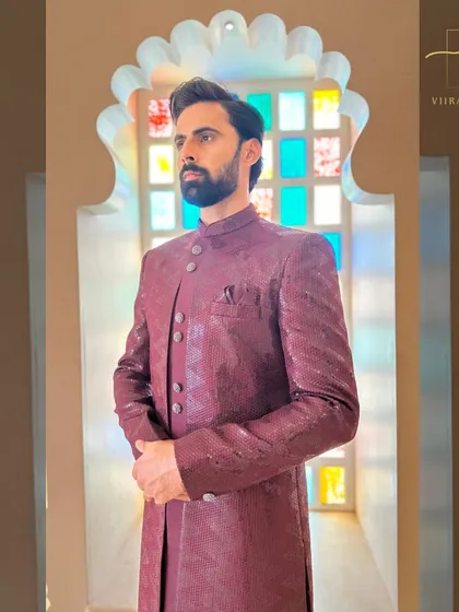 A side profile of the maroon sherwani, showing the clean tailoring and fit. We ensure every garment is crafted to your exact specifications.