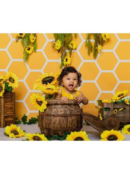 A baby girl expresses pure excitement from inside a wooden barrel, surrounded by sunflowers. Her animated expression brings so much life to this themed portrait.