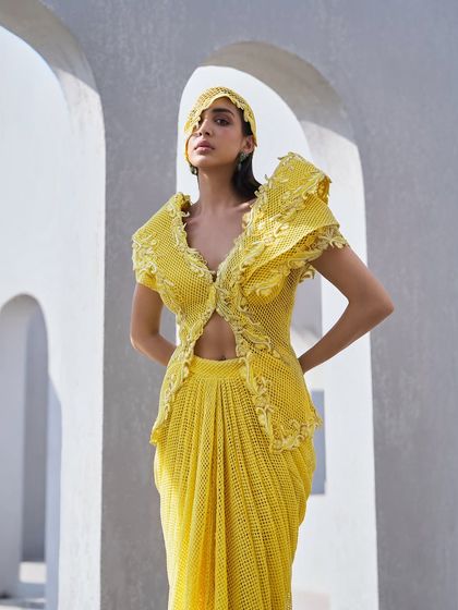 A structured mesh jacket in sunshine yellow, where light dances through its airy weave. Delicate floral embroidery unfurls across its surface, paired with a fluidly draped skirt.