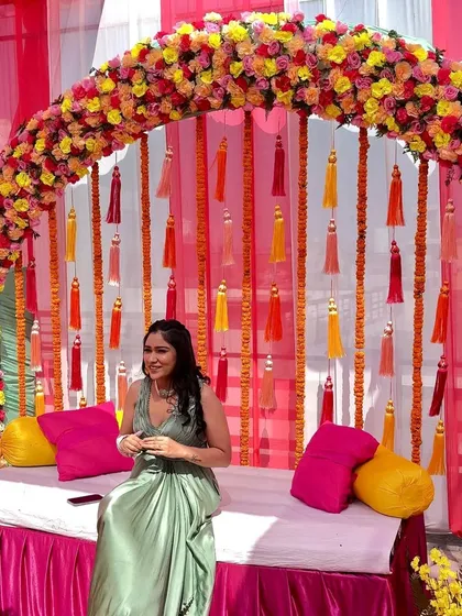A beautiful photo from a Mehandi ceremony, with the bride-to-be posing in front of our colorful floral arch and tassel backdrop.