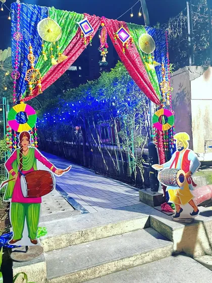 A traditional entrance gate for a Lohri or Punjabi-themed party. The colorful drapes are decorated with props and cutouts of a couple playing the dhol.