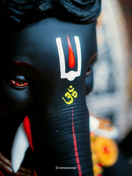 An extreme close-up on the face of the black Ganpati idol, focusing on the tilak and the 'Om' symbol. This perspective offers an intimate view of the divine artistry.