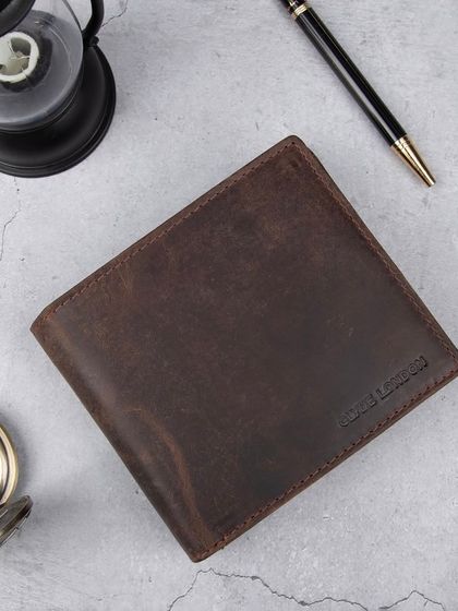A styled flat-lay of a distressed leather wallet with a pocket watch, pen, and lantern.