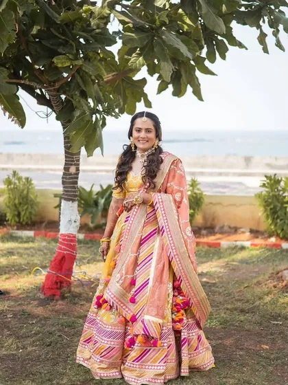 A collection from a beautiful Haldi ceremony. The bride's makeup is fresh and minimal, with a pop of color on the lips. Her hair is styled in a half-up, half-down look with braids, perfect for the fun and vibrant event.