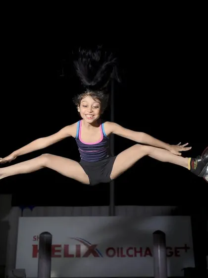 Capturing action requires perfect timing. For this shot of a young gymnast, I used a fast shutter speed and off-camera flash to freeze her mid-air split, highlighting her incredible flexibility and the power of the moment, even at a gas station at night.