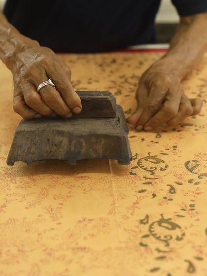 The hands of an artisan, weathered by decades of practice, gently press a vintage block onto fine silk. This is how we create our custom sarees, carefully mixing colors and curating blocks to match the rhythm of the weave.
