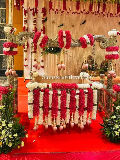For a naming ceremony, the cradle is the star. Here, we've decorated a beautiful silver cradle with garlands of red and white flowers, accented with delicate lotus buds, making it a perfect centerpiece for welcoming the new baby.