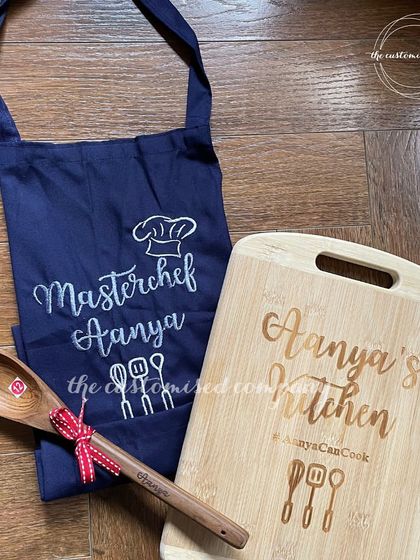 Create culinary magic with a personalized cook set. This gift for a young chef includes a custom-engraved "Aanya's Kitchen" chopping board, a matching spoon, and an embroidered "Masterchef" apron.