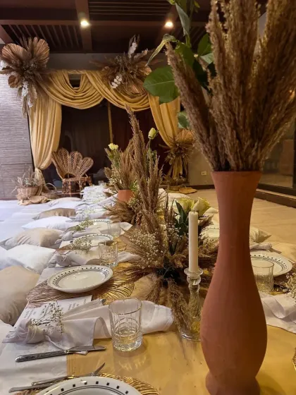 A close-up of the tablescape for the themed dinner. Terracotta vases with dried wheat, simple white plates, and candlelight create a rustic yet elegant look.