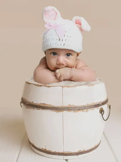 A minimalist portrait of a baby in a bunny hat, peeking over a rustic white barrel. This shows how a simple prop can create a very cute and memorable photo.