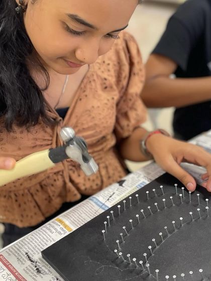 A young girl carefully hammers nails into her board, getting ready to create a Halloween-themed pumpkin string art.