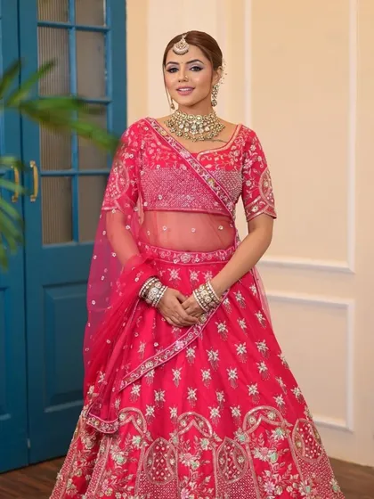 A full-length view of a bride in a stunning pink lehenga. The look is completed with a traditional kundan choker, maang tikka, and bangles, creating a classic and beautiful bridal statement.