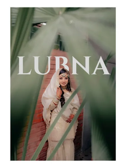 A beautiful solo portrait of the bride, Lubna, framed by green leaves, her traditional white attire and jewelry shining through.