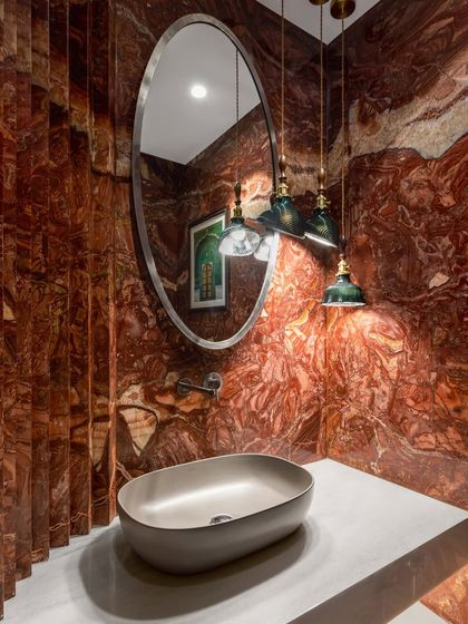 A full view of the dramatic red marble powder room. The fluted marble detail on the side adds another layer of texture, while the oval mirror and pendant lights create a sense of refined drama.