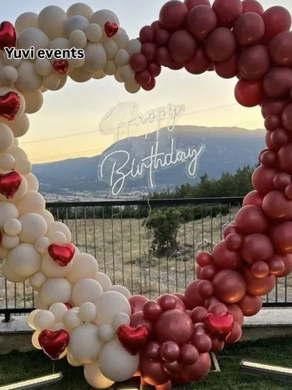 A heart-shaped balloon arch makes a perfect photo backdrop for any celebration. This one, designed for an outdoor birthday party, uses a two-tone design of white and maroon balloons with small red heart foils for an extra romantic touch.