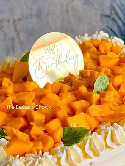 A close-up of the "Happy Birthday" topper on my mango cake, surrounded by fresh mangoes and mint leaves.