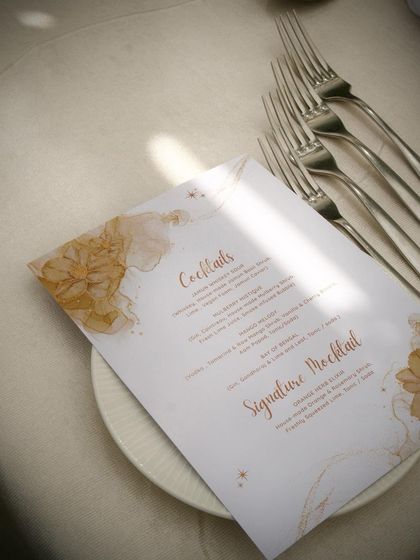 A custom cocktail menu resting on a plate, with elegant forks alongside it. The menu design reflects the sophisticated and artistic nature of the event.