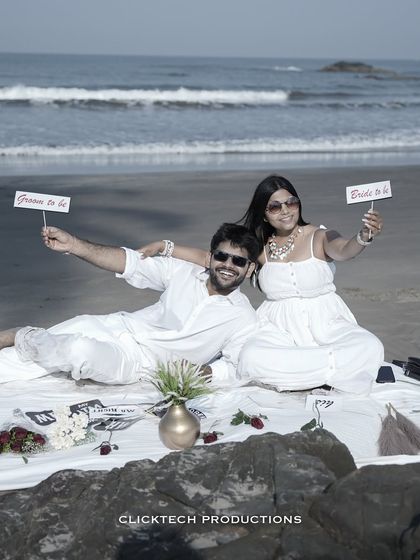 A fun picnic setup on a Goan beach, with the couple holding 'Groom to be' and 'Bride to be' signs.